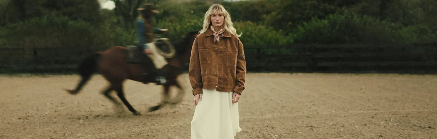 Jenna standing in a dirt field with a horse running in the background.