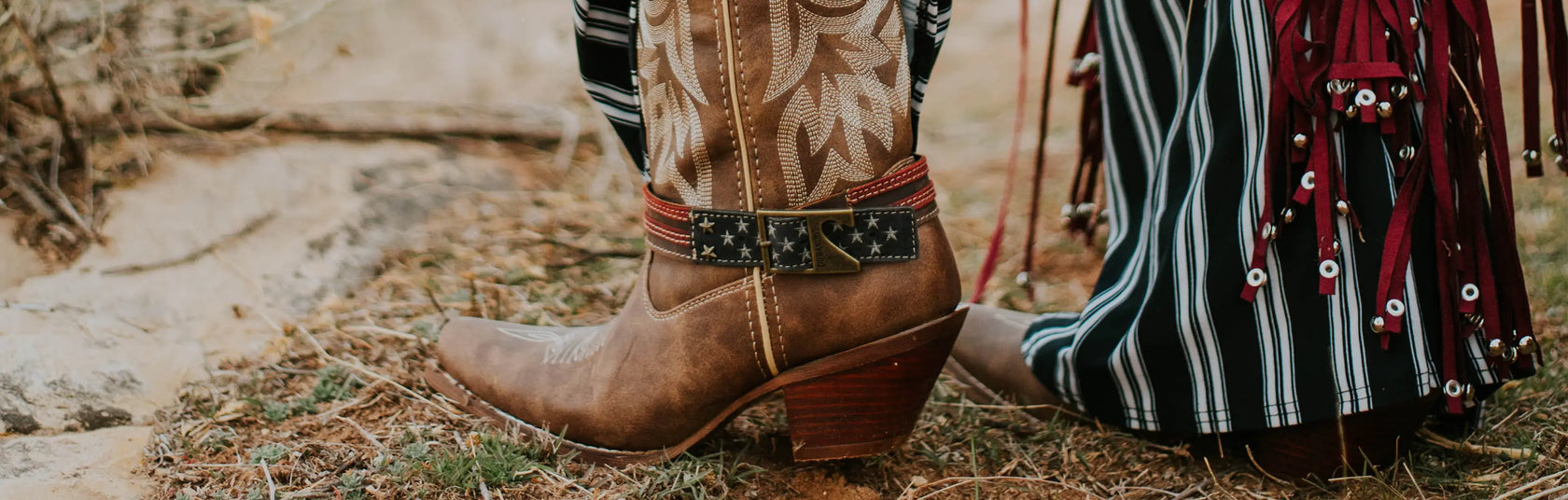 Close-up of brown Durango western boots with a patterned belt and striped pants on a natural background.