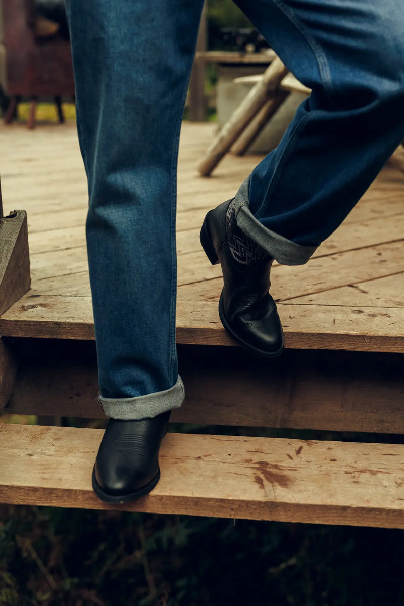 Person wearing black Durango cowboy boots and blue jeans standing on wooden steps.